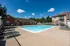 Inviting outdoor pool area in a serene apartment complex, featuring comfortable lounge chairs and surrounded by lush greenery and charming brick buildings.