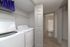 Modern laundry area with sleek washer and dryer adjacent to a bright bathroom, featuring neutral tones and elegant wood flooring.