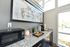 Bright kitchen nook with sleek granite countertop, stylish wooden cabinets, and modern appliances, enhanced by a large abstract painting and natural light from expansive windows.