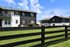 Charming modern apartments with sleek black and white facades, lush green lawns, and a serene blue sky backdrop.