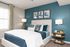 Modern bedroom with elegant blue accent wall, cozy white bed, stylish decor, and abundant natural light.
