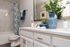 Modern bathroom featuring elegant white cabinetry, sleek marble shower walls, and stylish decor with a blue-patterned vase and lush greenery.