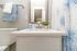 Bright and modern bathroom with sleek white countertop, elegant fixtures, and a stylish blue-and-white shower curtain.