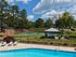 Inviting outdoor view featuring a sparkling swimming pool, tennis court, and charming gazebo surrounded by lush greenery under a clear blue sky.