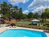 Inviting outdoor recreation area featuring a glistening pool, sun loungers, and tennis courts surrounded by lush greenery and tall trees.