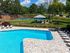 Elegant outdoor area featuring a sparkling swimming pool and adjacent tennis court, surrounded by lush greenery and stylish lounge chairs.