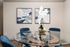 Elegant dining area featuring a modern glass table with plush blue chairs and contemporary abstract art on the walls, complemented by a chic orchid centerpiece.