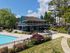Charming apartment complex showcasing a vibrant clubhouse with poolside seating, surrounded by lush greenery and a sparkling blue swimming pool under a clear sky.
