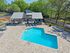 Inviting outdoor pool area with stylish lounge chairs, surrounded by lush greenery and a modern clubhouse under a clear blue sky.