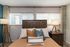 Cozy bedroom with elegant wooden headboard and chic accent pillows, featuring soft lighting from stylish floor lamps and natural light through large windows.