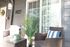 Charming apartment entrance with cozy wicker chairs, vibrant green plants, and elegant sliding glass door, creating a welcoming outdoor space.