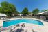 Inviting outdoor pool area with comfortable lounge chairs, surrounded by lush green trees and modern apartment buildings under a clear blue sky.