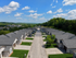 Charming suburban street view with modern townhouses, lush green lawns, and expansive skies, offering a serene community ambiance.