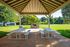 Charming outdoor pavilion with picnic tables and a stone grill set in a lush, green park offering serene relaxation.