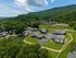 Charming aerial view of a tranquil apartment community nestled in lush greenery with convenient pathway access and a picturesque backdrop of rolling hills and a church.