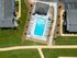 Aerial view of a luxurious apartment complex featuring a sparkling swimming pool with sun loungers and umbrellas, surrounded by well-manicured lawns and walking paths.