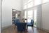 Bright dining area with modern blue chairs around a glass table, set against floor-to-ceiling windows and stylish geometric curtains.