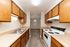Charming galley kitchen with wooden cabinets, modern stovetop, double sinks, and ample countertop space, leading into a cozy dining area with elegant lighting.