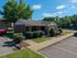 Charming red-brick single-story house with manicured landscaping, set against a backdrop of lush greenery and clear blue skies.