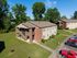 Charming residential complex with brick facade and well-maintained grounds, featuring large windows and ample parking, surrounded by lush greenery.