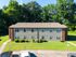Charming two-story apartment building with red brick accents, surrounded by lush greenery, offering ample parking space in a serene setting.