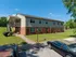 Charming two-story apartment building with brick facade and lush green surroundings, offering spacious outdoor areas and easy access via exterior staircase.