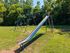 Charming playground with a classic slide and swings, set amidst lush greenery for outdoor enjoyment.