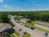 Charming residential community with multiple apartment buildings nestled in lush greenery, ample parking space, and serene surroundings under a clear blue sky.