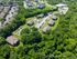 Aerial view of a serene apartment complex surrounded by lush greenery, showcasing spacious parking and well-maintained buildings.