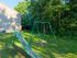 Charming backyard playground with a green slide and swing set, surrounded by lush trees and vibrant greenery.