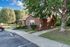 Charming brick home surrounded by lush greenery and a well-maintained lawn, with convenient parking and tree-lined paths.