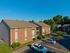 Charming brick apartment building with lush greenery and ample parking, set against a clear blue sky.