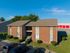 Charming red brick apartment building with well-maintained landscaping and ample parking, set against a clear blue sky.