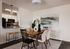 Elegant dining area with modern wooden table, stylish chairs, and artistic decor, overlooking a chic open kitchen with sleek appliances.