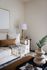 Chic living room with a cozy cream sofa, stylish pillows, a textured throw, modern wooden lamp, and elegant decor on a patterned rug.