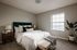 Bright and inviting bedroom featuring a plush bed with a green headboard, elegant bedside tables, and a tall potted plant by the window.