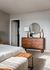 Elegant bedroom featuring a modern wooden dresser with decorative vases, a round mirror, and cozy white bedding.