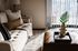 Inviting living room with a cozy beige sofa and elegant decor, bathed in natural light through glass doors with vertical blinds.