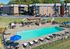 Charming apartment complex with inviting outdoor pool area, surrounded by lush greenery and comfortable lounge chairs under blue umbrellas.