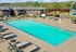 Inviting outdoor pool area with lounge chairs and a pergola, surrounded by lush greenery and modern apartments.