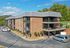 Charming three-story brick apartment building with spacious balconies, lush trees, and ample parking on a sunny day.