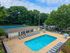 Inviting outdoor complex featuring a sparkling swimming pool, ample lounge chairs, adjacent sports court, and lush green surroundings.