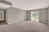 Bright and spacious living room with plush carpet and sliding glass doors leading to a serene balcony view.
