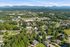 Scenic aerial view of a lush, green residential area surrounded by picturesque mountains and abundant greenery, offering tranquil living.