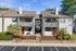 Charming two-story apartment building with vibrant red doors and decorative balconies, surrounded by lush landscaping and ample parking space.