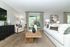 Bright, modern living room featuring a cozy white sofa, elegant decor, and large windows with lush green views.
