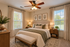 Inviting and elegant bedroom featuring a plush bed with stylish green accents, framed botanical art, and natural sunlight streaming through large windows.