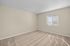 Bright second bedroom with plush carpet and large window offering natural light and serene views.