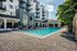 Luxurious apartment complex with a pristine swimming pool, stylish lounge chairs, and elegant balconies under a bright sky.