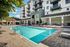 Luxurious apartment complex with a pristine pool, stylish sun loungers, and modern architecture surrounded by lush greenery.
